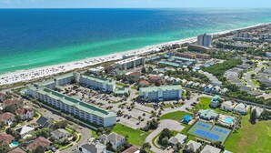 An aerial view of a coastal resort area with beachfront properties, a large hotel complex, and a swimming pool.