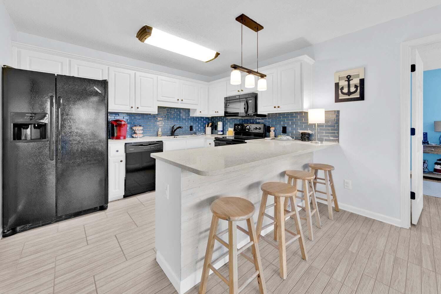 Una cocina moderna con armarios blancos, un refrigerador negro, una isla integrada con taburetes y un salpicadero de azulejos azules.