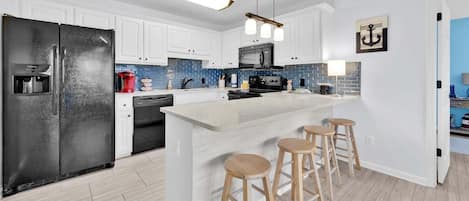 Una cocina moderna con armarios blancos, un refrigerador negro, una isla integrada con taburetes y un salpicadero de azulejos azules.