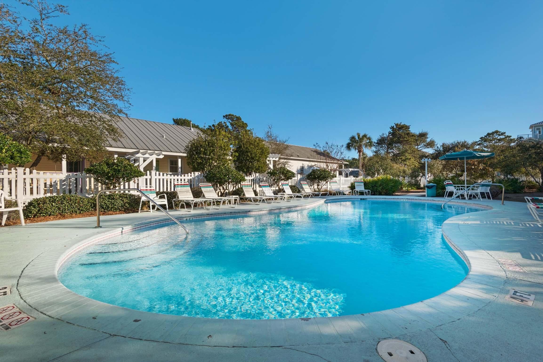 A swimming pool with lounge chairs and a white picket fence.