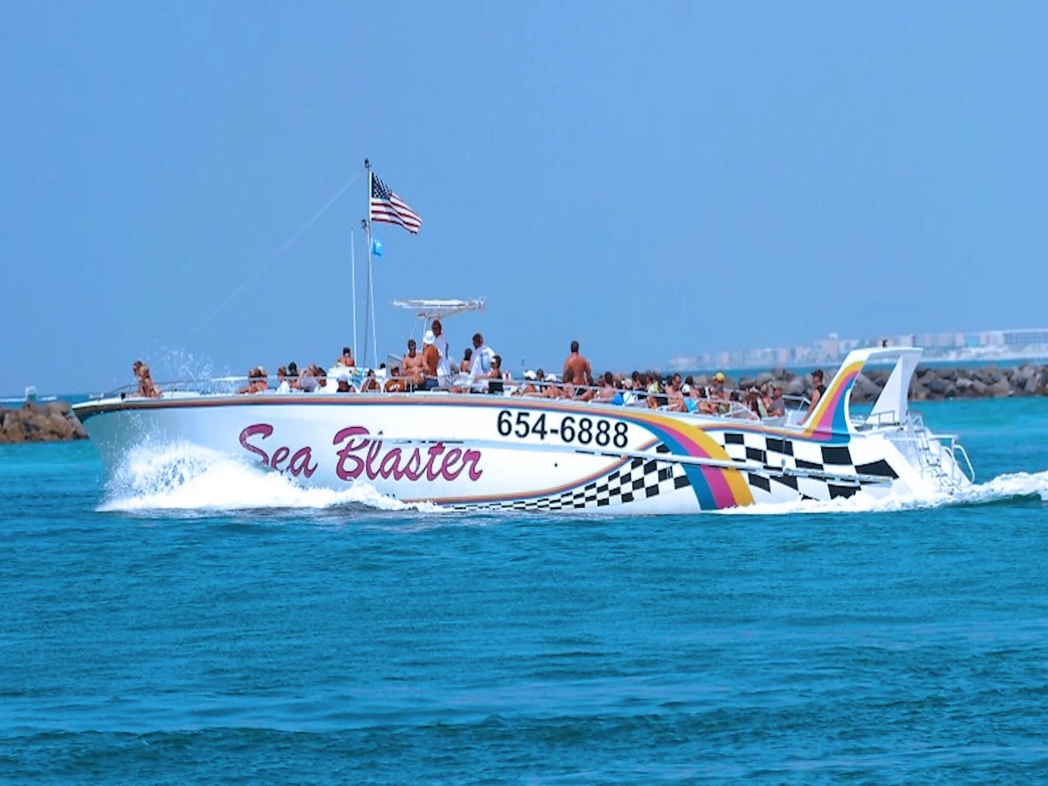 Ein Schnellboot mit dem Namen 'Sea Blaster', mit Karomuster und Regenbogenstreifen, fährt auf dem Wasser.
