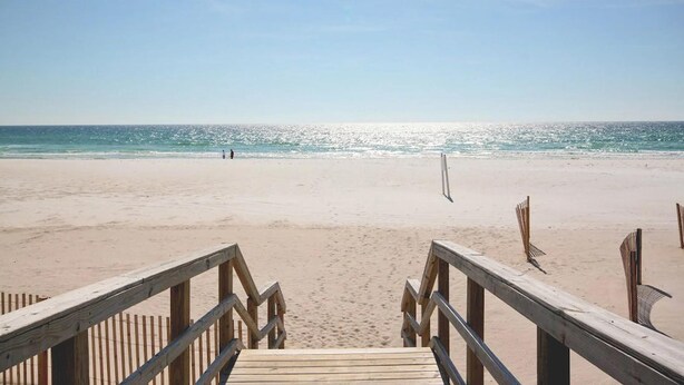 A wooden boardwalk leading to a beach with a volleyball net.