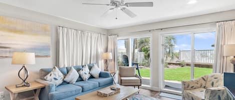 A living room with a blue sofa, a wooden coffee table, a beige armchair, and a ceiling fan.