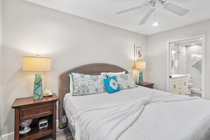 A bedroom with a bed, two bedside tables, a ceiling fan, and a bathroom visible through an open door.
