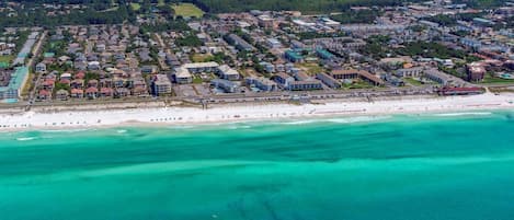 An aerial view of a coastal town with a beachfront, residential buildings, and a marina.