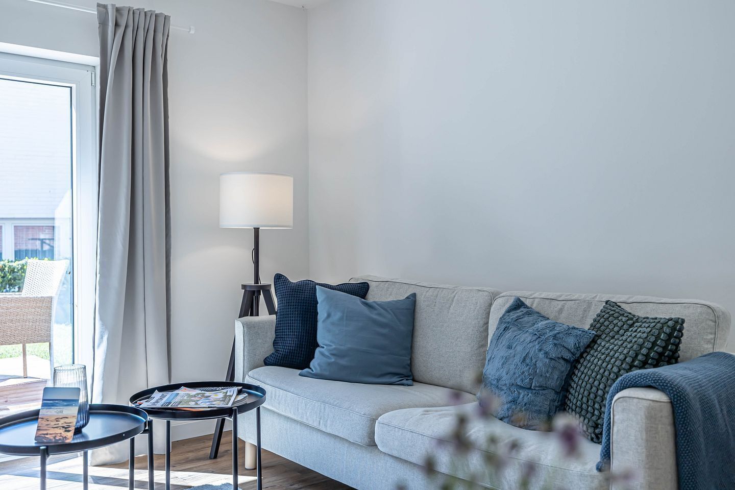 Ett modernt vardagsrum med en grå soffa, en golvlampa och ett litet bord med en tidning på.