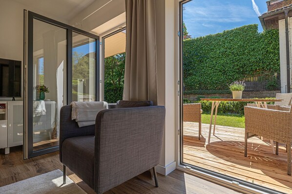 A modern living room with a grey sofa, a glass door leading to an outdoor patio with wicker furniture and a table. - Fewo1846 - Lille Loft - Fewo1846 - Lille Loft / Ebenerdiges Apartment mit 2 Schlafzimmern und Garten (Glücksburg (Ostsee))
