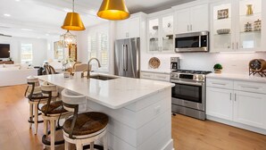 A modern kitchen with white cabinetry, stainless steel appliances, and a central island with bar stools. - Once Upon a Tide (Miramar Beach)