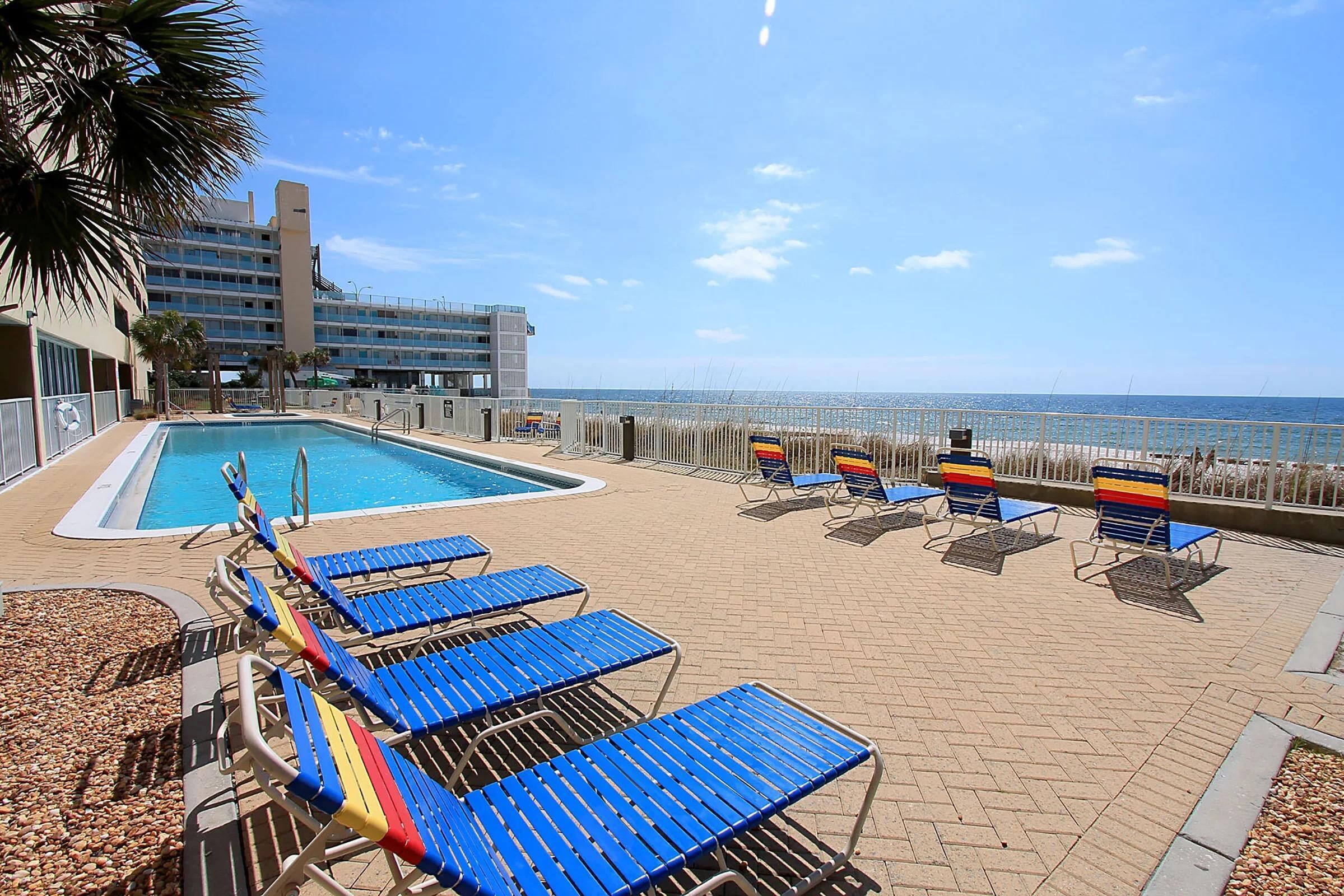 A pool area with lounge chairs and a view of the ocean.