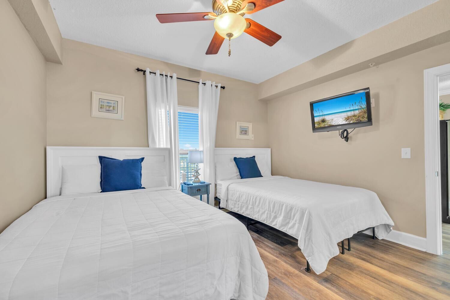 A hotel room with two beds, a ceiling fan, a TV, and a window with curtains.