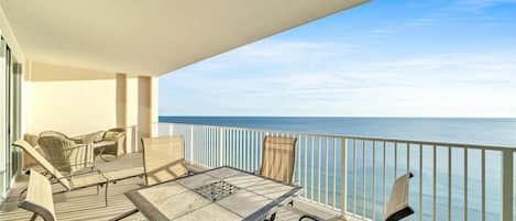 A balcony with a table and chairs, overlooking a calm sea.