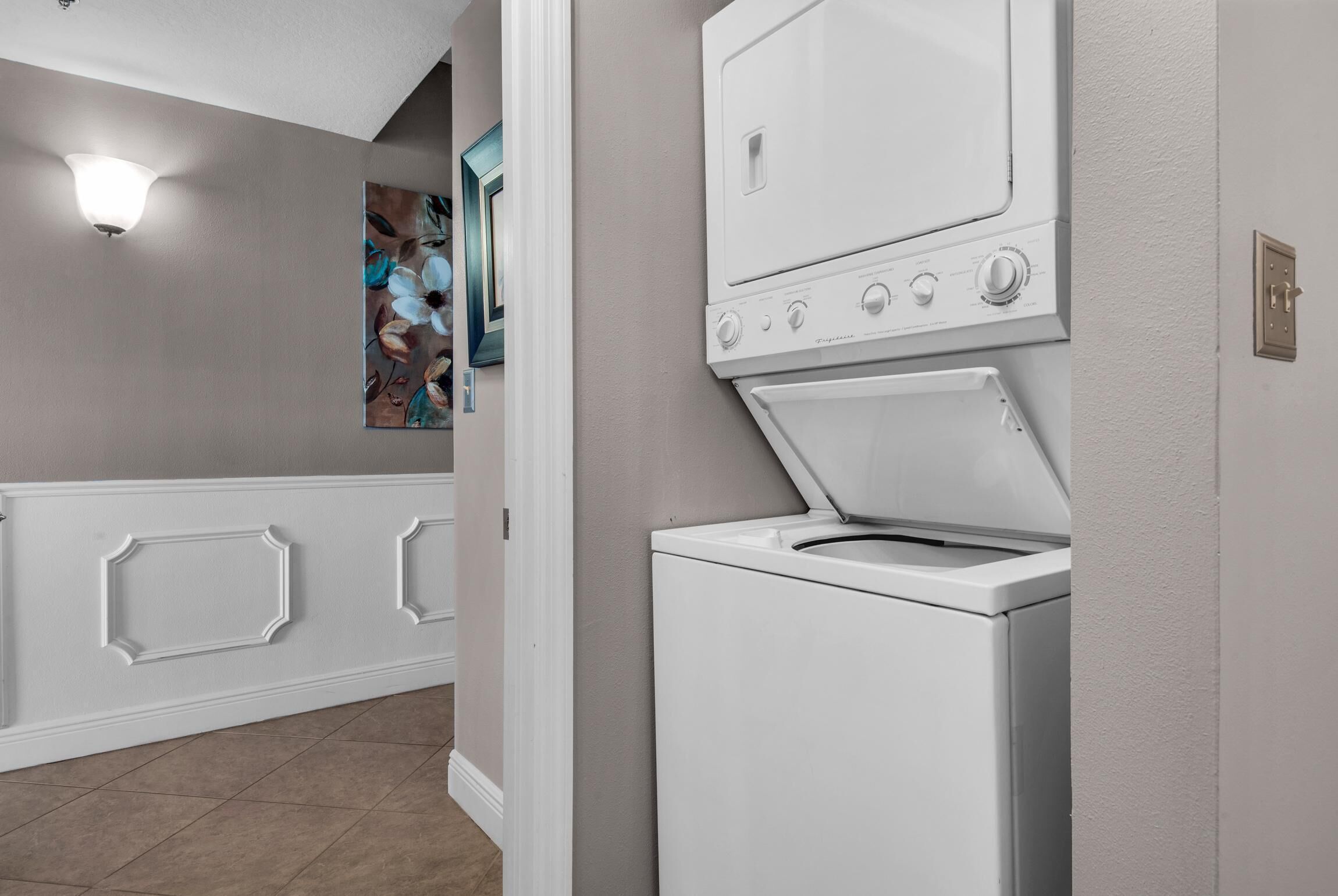 Une buanderie équipée d’un lave-linge et d’un sèche-linge superposés, d’un luminaire et d’un élément décoratif mural.