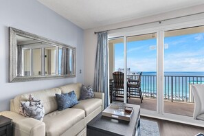 En stue med sofa, sofabord og et stort spejl. Der er en balkon med udsigt over havet.