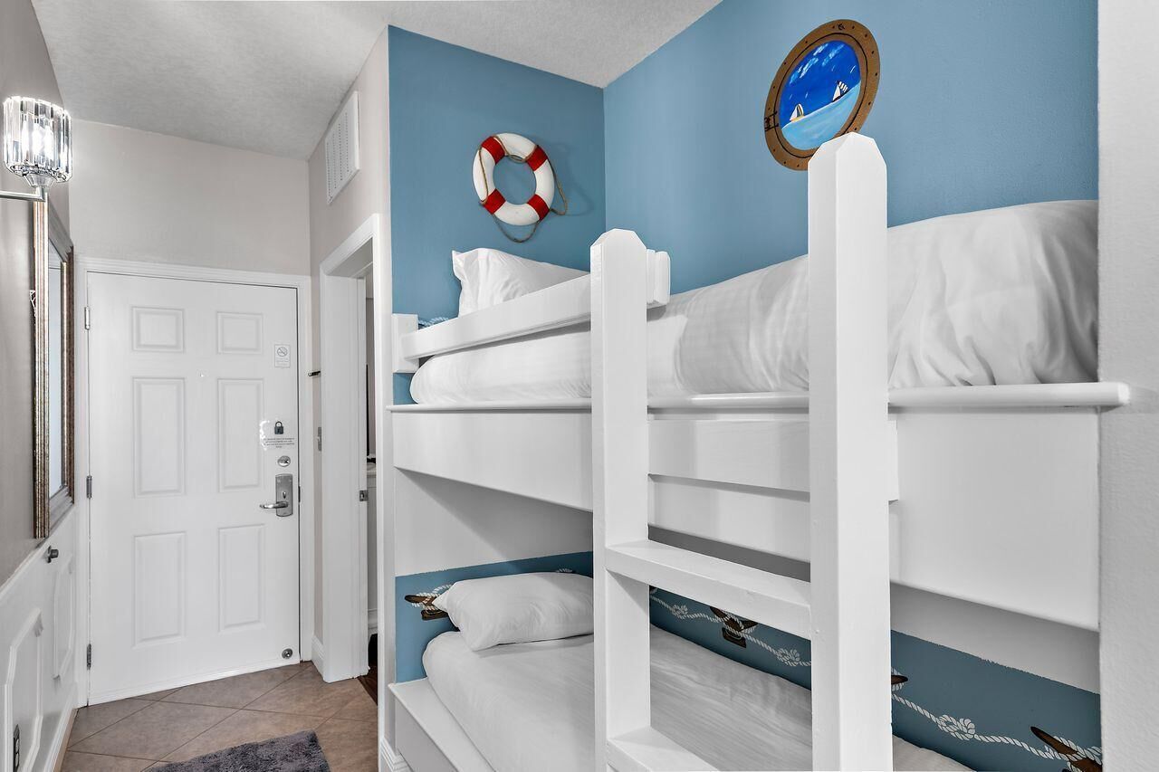 A room with bunk beds, a door, a life preserver, and a round window with a view.