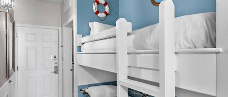 A room with bunk beds, a door, a life preserver, and a round window with a view.