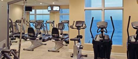 Un gimnasio con diferentes máquinas de cardio, un espejo grande y una pantalla de televisión.