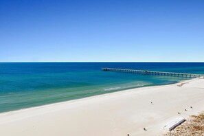 A beach with a pier extending into the ocean, sandy shore, and clear blue sky. - Sterling Reef 705 (Panama City Beach)