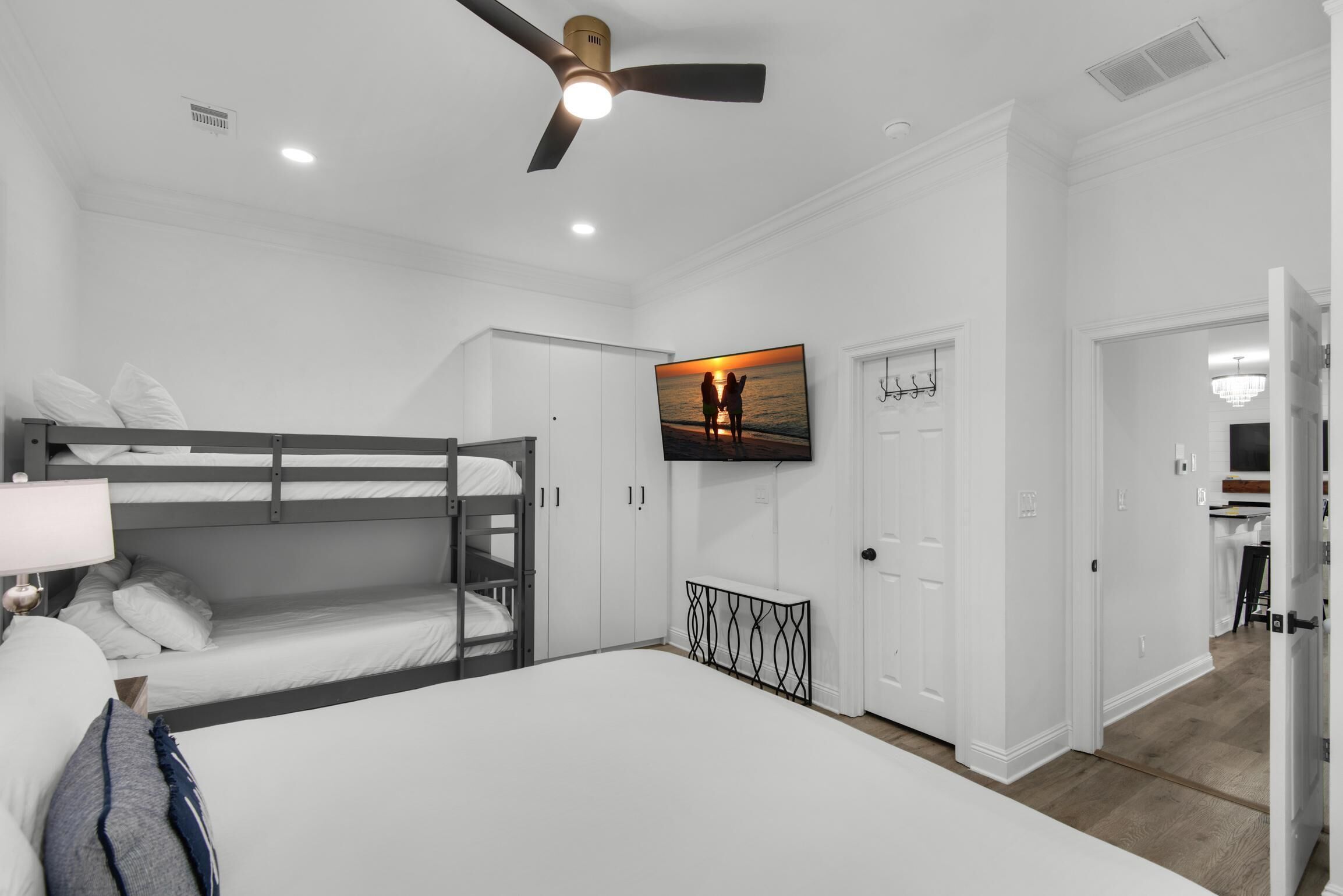 Une chambre avec des lits superposés, un ventilateur de plafond, un téléviseur fixé au mur et une porte donnant sur une autre pièce.