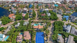 Vista aérea de una zona residencial con casas, una cancha de tenis y una playa al fondo.