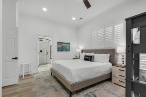 A bedroom with a bed, bedside table, nightstand, and a door leading to a bathroom. - Catch of the Day (Destin)