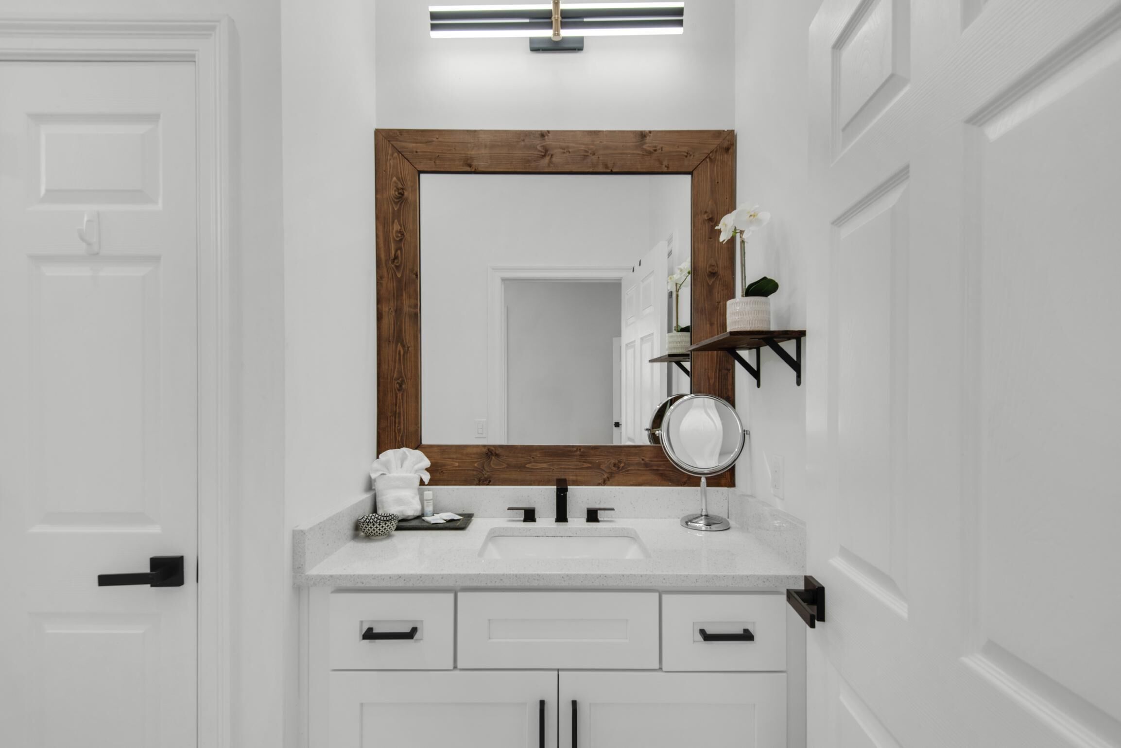 Une salle de bain avec un meuble-lavabo blanc, un miroir encadré en bois et une étagère contenant des articles de toilette.
