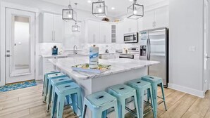 A modern kitchen with white cabinets, a central island with stools, stainless steel appliances, and pendant lighting. - Sea Ya Sun (Miramar Beach)
