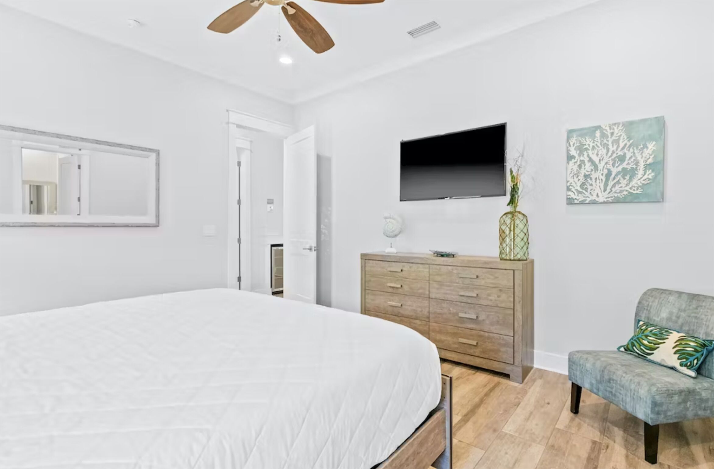 A bedroom with a large bed, a wooden dresser, a TV mounted on the wall, and a chair.