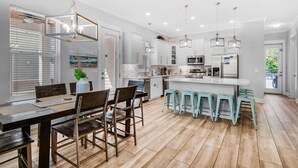 A modern kitchen with white cabinets, a central island with stools, and pendant lighting. - Sea Ya Sun (Miramar Beach)