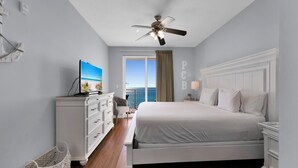 A hotel room with a bed, a dresser, a television, a ceiling fan, and a view of the ocean.