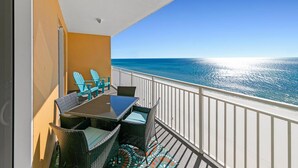 A balcony with a view of the ocean, a table with chairs, and a patterned rug.