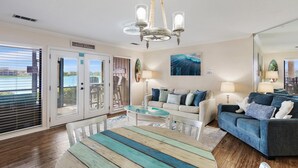 A living room with a wooden coffee table, two sofas, a chandelier, and a large window with blinds. - Seascape Lakefront Villas 189- Don't Worry, Beach Happy (Miramar Beach)