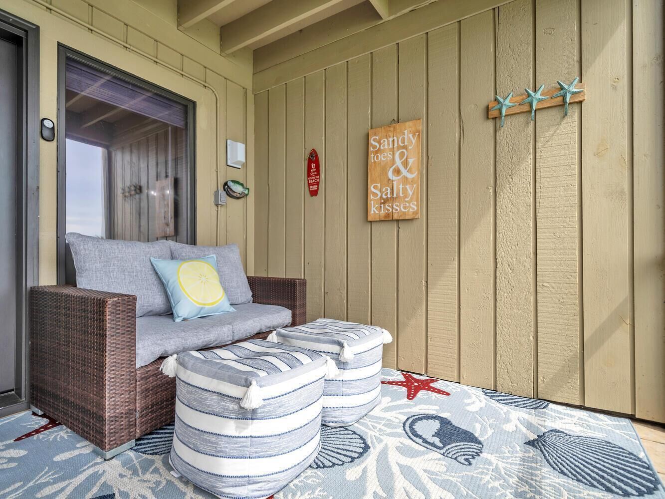 A cozy outdoor seating area with a wicker sofa, striped ottomans, and a nautical-themed rug.