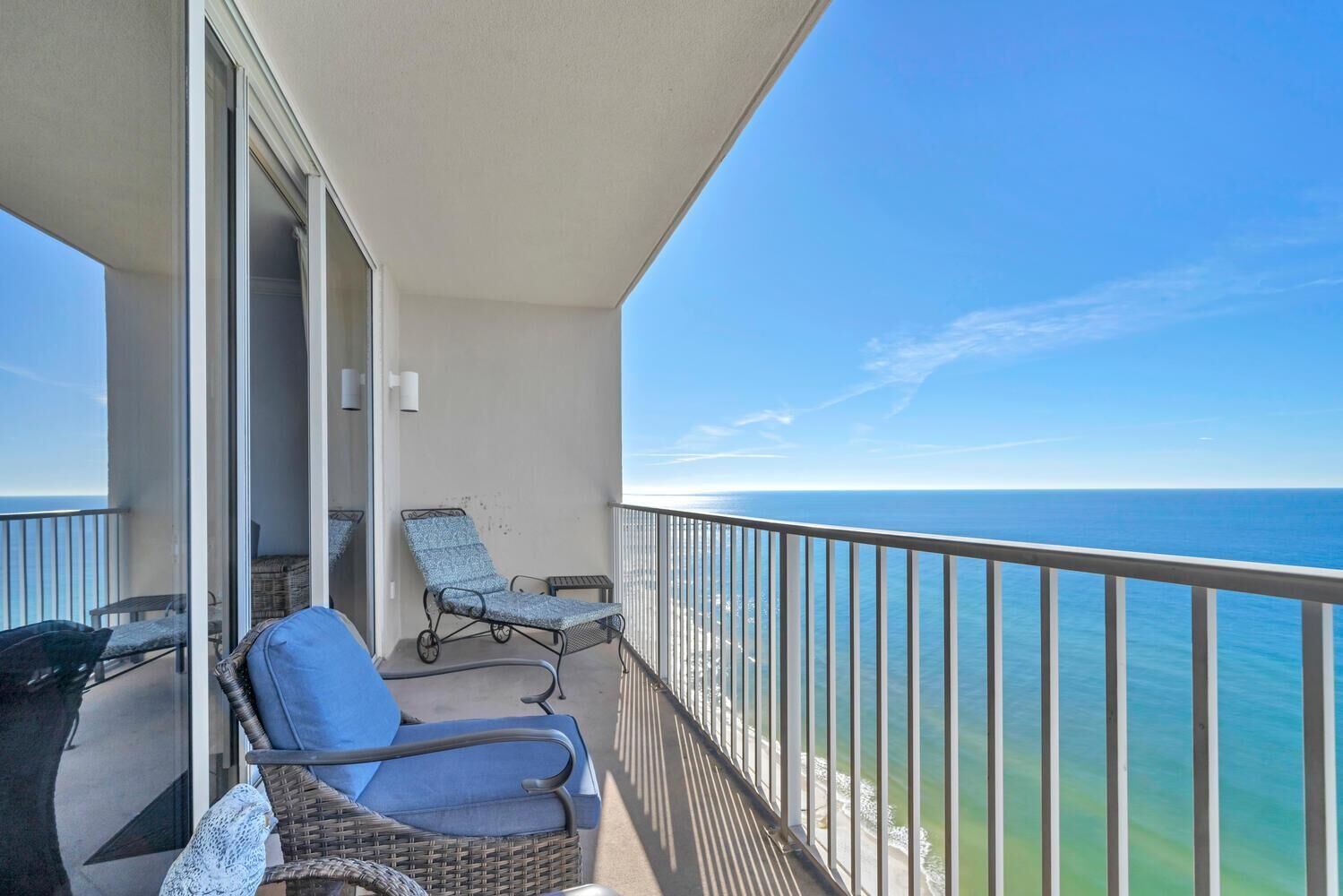 A balcony with two wicker chairs and a table, overlooking a clear blue sea.