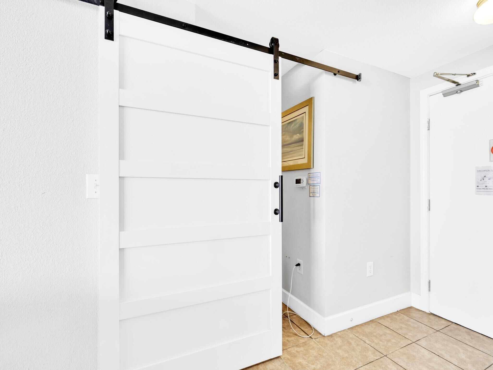 Un couloir avec une porte coulissante, un tableau encadré au mur et une pancarte sur la porte.