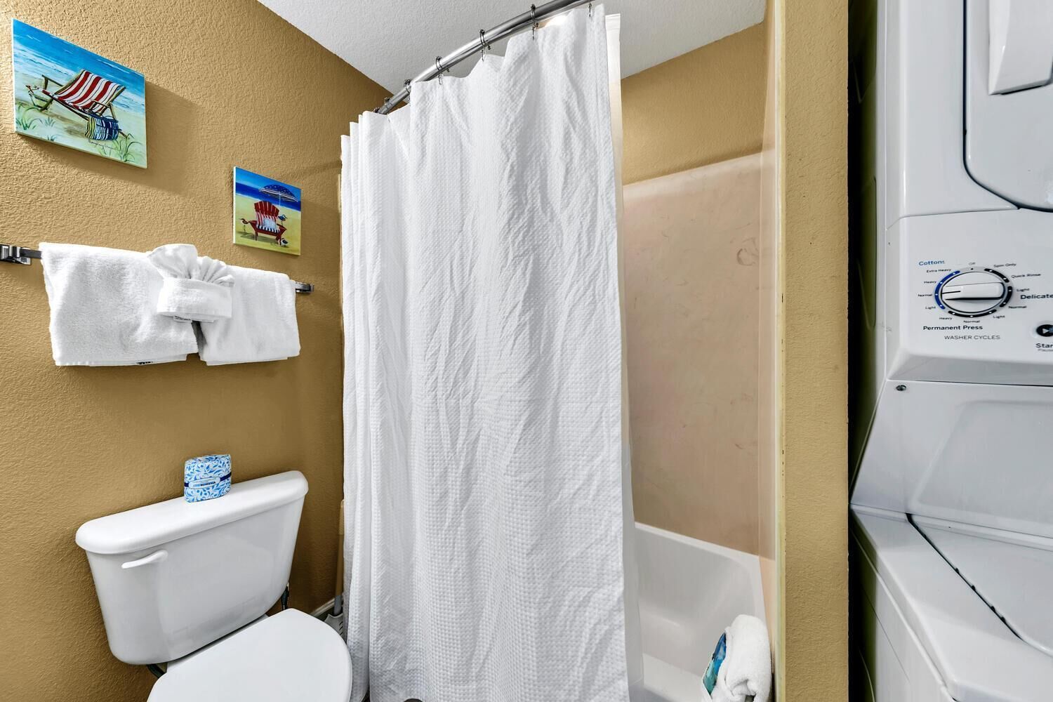 A bathroom with a toilet, a shower curtain, a towel rack with towels, and a washing machine.