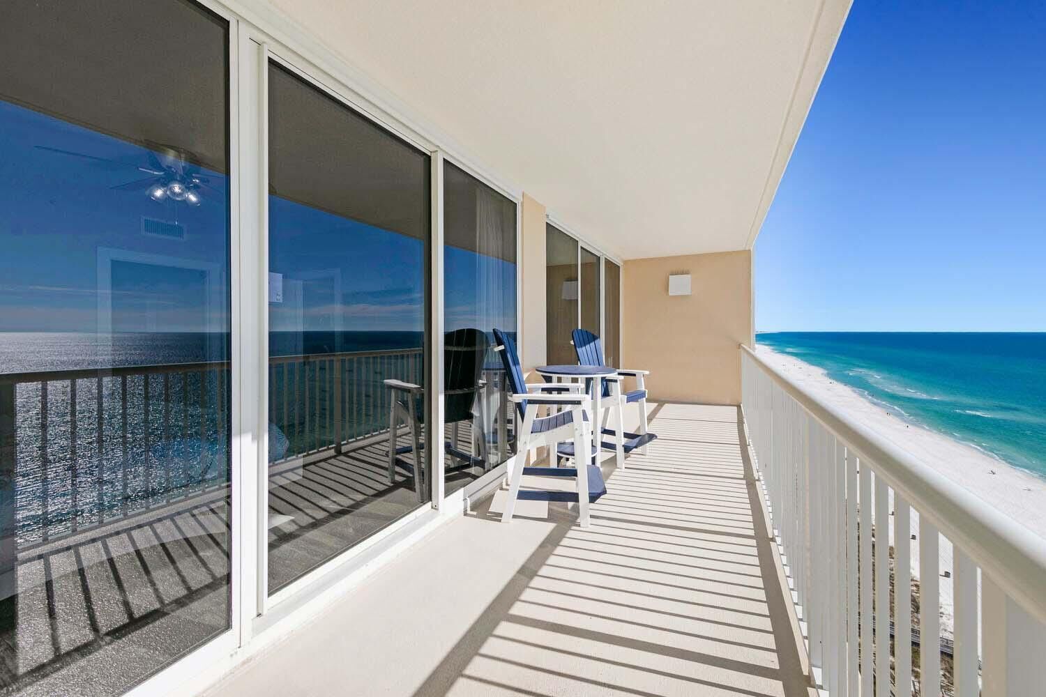 A balcony with a view of the ocean, a table with chairs, and a ceiling fan.