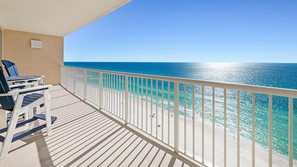 A balcony with a view of the ocean, a white railing, and two blue chairs.