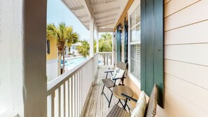 Un balcon abrité, équipé de deux chaises et d’une petite table, qui offre une vue sur une piscine et des palmiers.