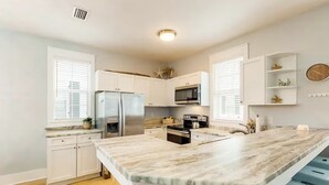 Une cuisine moderne avec des meubles blancs, un grand îlot central doté d’un plan de travail en marbre et un four à micro-ondes encastré.