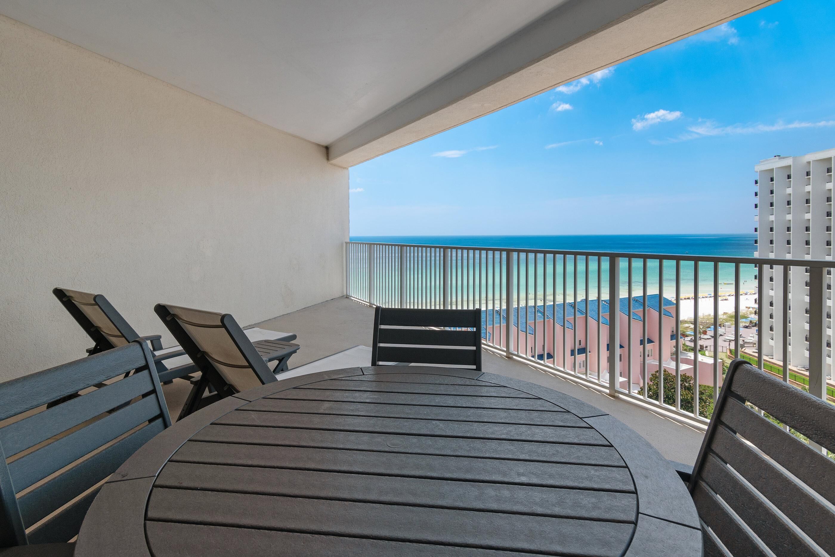 A balcony with a table and chairs, overlooking a beach and buildings.