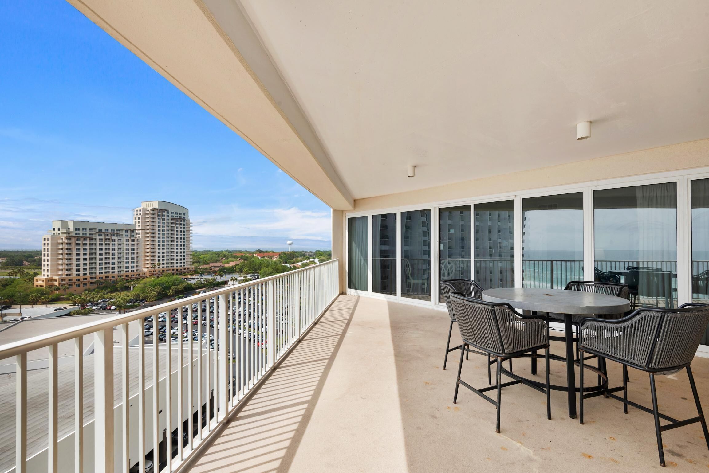 A balcony with a table and chairs, overlooking a parking lot and buildings.
