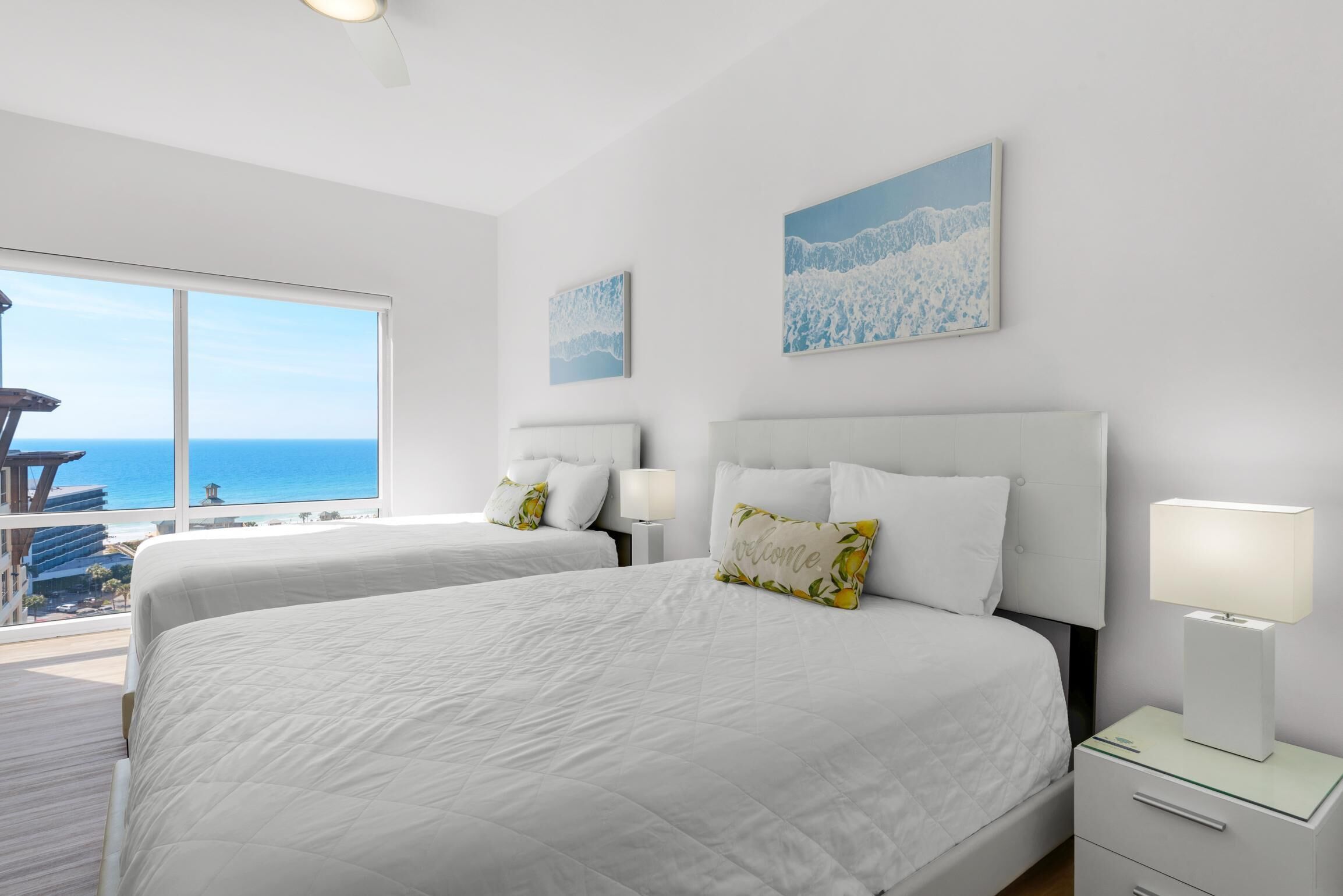 A hotel room with two beds, a balcony with a view of the sea, and artwork on the walls.