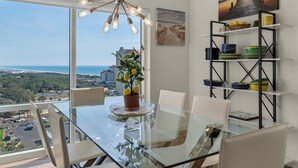 A dining area with a glass table, white chairs, a potted plant, and a view of the ocean. - Luau I 7103 (Miramar Beach)