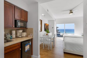 A modern kitchen with a microwave, coffee maker, and dishwasher. There is a dining area with a table and chairs, and a bed with a view of the ocean. - Luau Retreat (Miramar Beach)