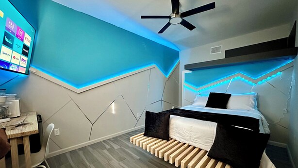 Un dormitorio moderno con una cama, un escritorio y un ventilador de techo.
