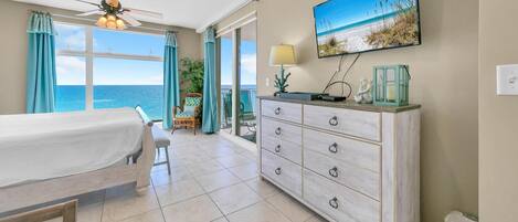 A room with a bed, a dresser, a ceiling fan, a TV, and a view of the ocean.