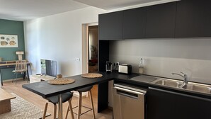 A modern kitchen with black cabinets, stainless steel appliances, and a wooden dining area. - La Voile du Rocher (Nouméa)