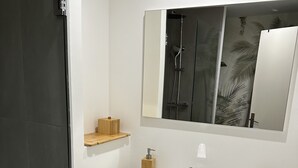 A modern bathroom with a white sink, a mirror, and a shower. There are wooden storage boxes and a towel rack. - La Voile du Rocher (Nouméa)
