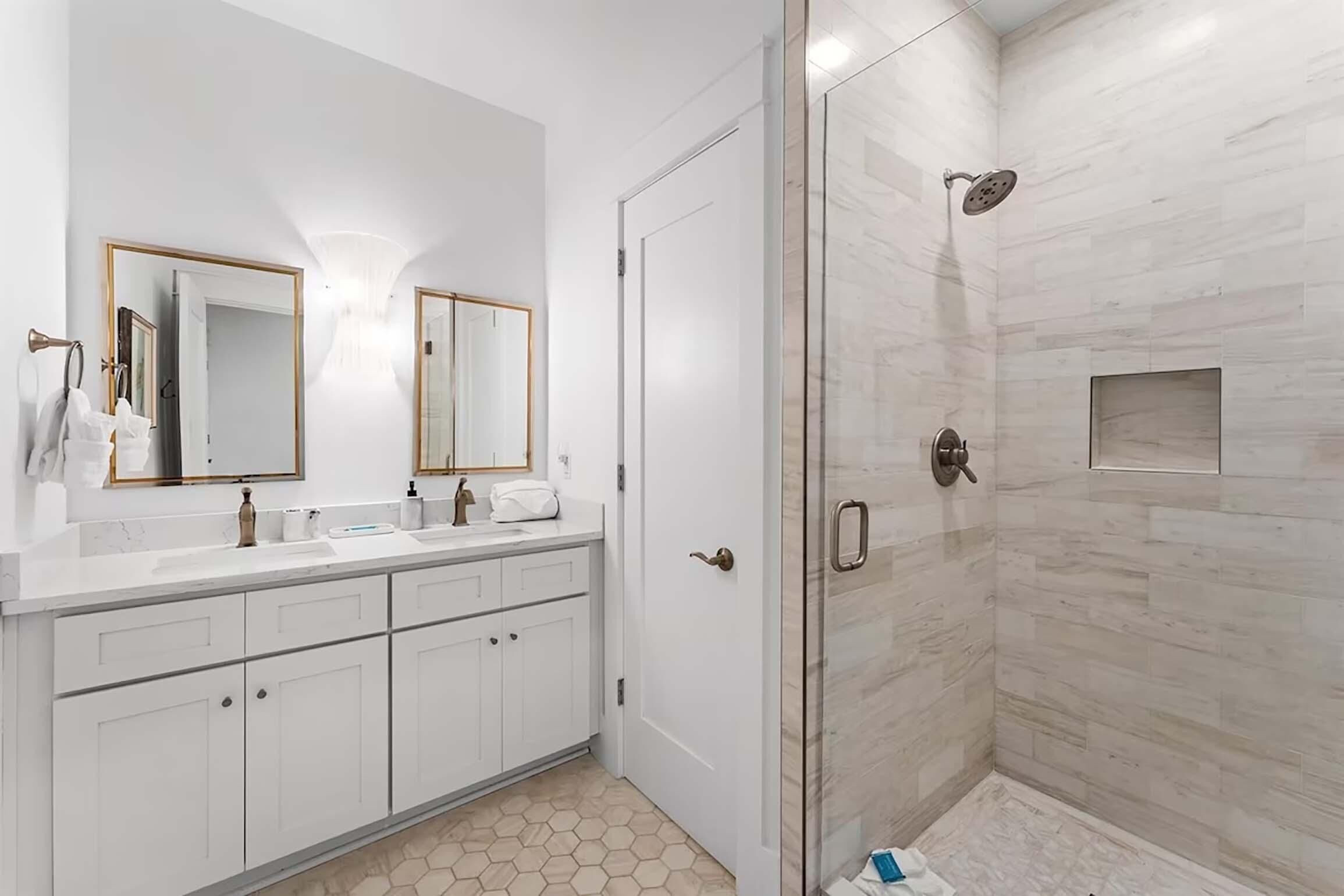 A modern bathroom with a glass-enclosed shower, white cabinetry, and a large mirror.