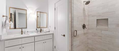 A modern bathroom with a glass-enclosed shower, white cabinetry, and a large mirror.